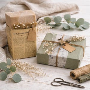 May include: Two wrapped gifts with decorative elements. One is wrapped in brown paper with a newspaper-style band and a tag. The other is wrapped in green paper with a newspaper-style band and a tag. Both are adorned with dried flowers and twine.