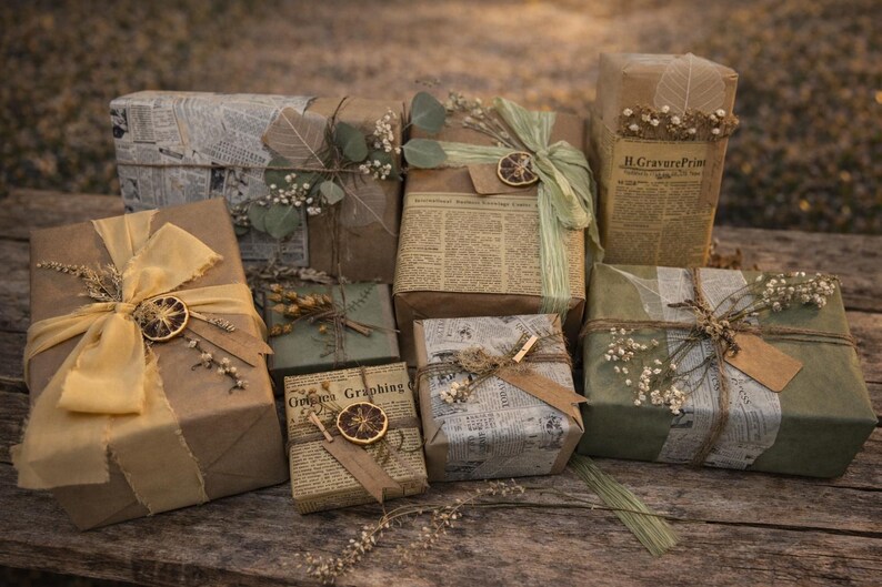 May include: An assortment of wrapped gifts on a wooden surface. The gifts are wrapped in brown paper, newspaper, and olive green paper, adorned with dried flowers, ribbons, and dried orange slices. Some gifts have tags.
