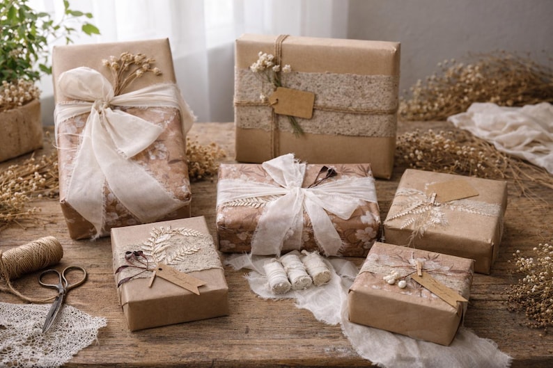 May include: Several gift boxes wrapped in brown paper, adorned with ribbons, lace, and dried flowers. Some boxes have tags. A pair of scissors and twine are also visible, suggesting a craft or gift-wrapping theme.