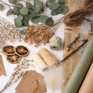 May include: An assortment of craft supplies including dried flowers, twine, paper rolls, and tags. The image features eucalyptus leaves, dried orange slices, and rolls of twine and paper. Several tags read "Thank you".