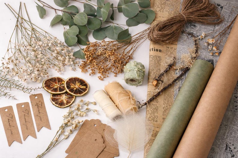May include: An assortment of craft supplies including dried flowers, twine, paper rolls, and tags. The image features eucalyptus leaves, dried orange slices, and rolls of twine and paper. Several tags read "Thank you".