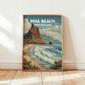 Op de afbeelding: Een ingelijste kunstdruk van Piha Beach, Nieuw-Zeeland. Het kunstwerk toont een kustlandschap met een grote rotsformatie, een zandstrand en oceaangolven. De lucht is blauw met pluizige wolken. De tekst "PIHA BEACH NEW ZEALAND" staat bovenaan.