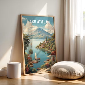 May include: A framed print of Lake Atitlan, depicting a scenic view with a lake, boats, and a mountain. The print is propped against a wall beside a small white stool and a round, beige floor cushion. The text "LAKE ATITLAN" is at the top.