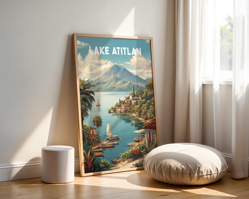 May include: A framed print of Lake Atitlan, depicting a scenic view with a lake, boats, and a mountain. The print is propped against a wall beside a small white stool and a round, beige floor cushion. The text "LAKE ATITLAN" is at the top.