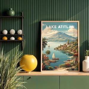 May include: A framed print of Lake Atitlan, depicting a tranquil lake scene with sailboats, a mountain backdrop, and a village. The print has a light wood frame and is displayed on a green cabinet. The text "LAKE ATITLAN" is at the top.