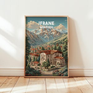 Könnte beinhalten: Ein gerahmter Kunstdruck mit dem Text "IFRANE MOROCCO" über einer malerischen Ansicht einer Stadt in einem Tal. Das Kunstwerk zeigt Gebäude mit roten Ziegeldächern, umgeben von üppigem Grün und Bergen im Hintergrund.