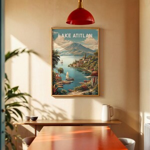 May include: A framed print of Lake Atitlan, depicting a scenic view of the lake, mountains, and buildings. The print has a gold frame and is hanging on a beige wall. The text "LAKE ATITLAN" is at the top of the print.