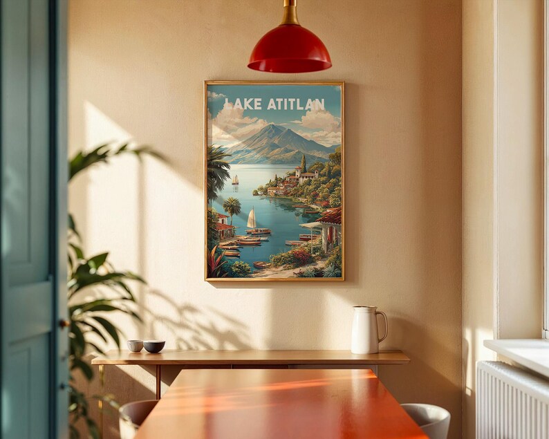 May include: A framed print of Lake Atitlan, depicting a scenic view of the lake, mountains, and buildings. The print has a gold frame and is hanging on a beige wall. The text "LAKE ATITLAN" is at the top of the print.