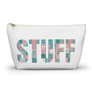 May include: White zippered pouch with the word "STUFF" in a patchwork design. The letters are composed of various floral and geometric patterns in shades of pink, teal, and green. A gold zipper closure is visible.