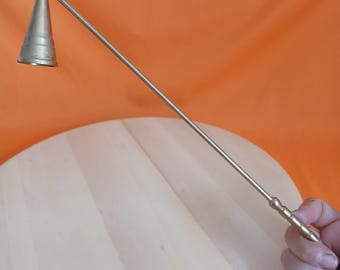 May include: A silver candle snuffer with a conical bell and a long, slender handle. The handle has a decorative, textured grip. The snuffer is designed to extinguish candles safely and efficiently.
