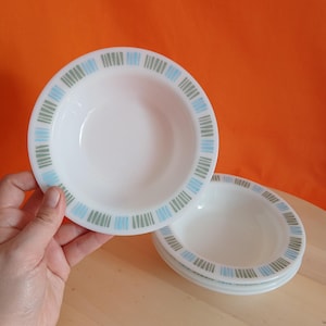 May include: White ceramic bowls with a blue and green striped pattern around the rim. One bowl is held up, with three more stacked below. The bowls have a simple, clean design, suitable for serving soups or desserts.