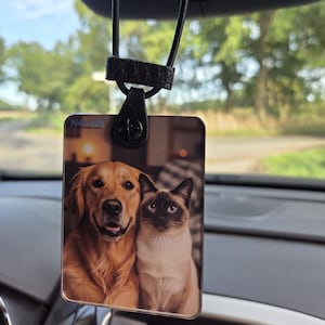 Puede incluir: Ambientador rectangular para coche con un Golden Retriever y un gato siamés. El ambientador está suspendido por un cordón elástico negro y un clip. La palabra "NAVIMIT" es visible en la parte superior del ambientador.