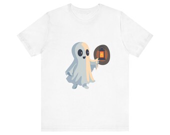 May include: White t-shirt featuring a cartoon ghost holding a lantern. The ghost is light gray with a friendly expression and a tan glow. The lantern is orange and black, set against a brown background.