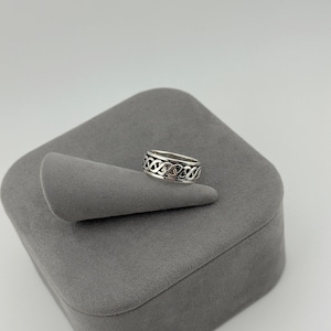 May include: A silver ring featuring a continuous, intricate woven knot pattern around the entire band. The metal has a polished finish with darkened recessed areas that highlight the detailed, repeating interlaced design of the metalwork.