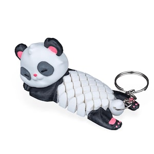 May include: A white and black panda keychain lying down, with a silver keyring attached. The panda has black ears, eye patches, and paws, with pink accents on the ears and feet. The panda's body is made of white, rectangular segments.