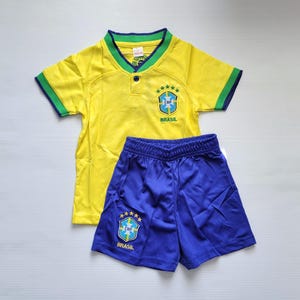 May include: A yellow and blue Brazilian soccer uniform set. The yellow jersey has green and blue trim, a CBF logo, and the word "BRASIL". The blue shorts also feature the CBF logo and the word "BRASIL".