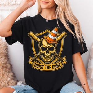 May include: Black t-shirt featuring a gold skull wearing an orange and white traffic cone, with crossed baseball bats behind it. The design includes a gold shield and the text "HOIST THE CONE" in a banner.