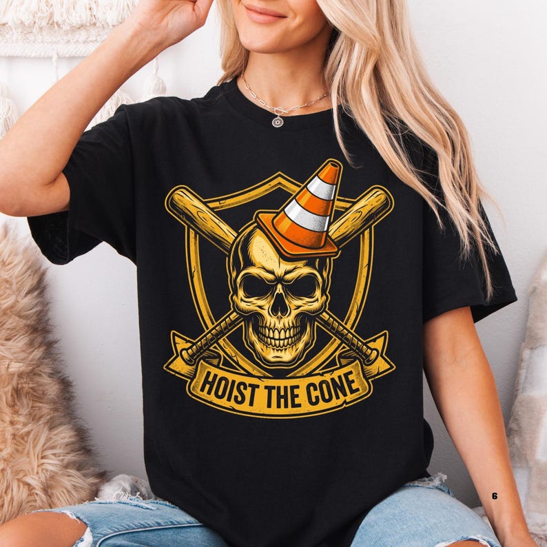 May include: Black t-shirt featuring a gold skull wearing an orange and white traffic cone, with crossed baseball bats behind it. The design includes a gold shield and the text "HOIST THE CONE" in a banner.
