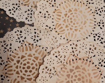 May include: A collection of cream-colored paper doilies with intricate, openwork designs. The doilies have a circular shape with a central floral pattern and scalloped edges. The background is a dark surface with small gold stars.