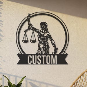 Puede incluir: Arte mural de metal negro que representa a la Justicia sosteniendo una balanza, enmarcado por un círculo y una pancarta con la palabra "CUSTOM". La obra de arte se exhibe en un balcón con plantas, faroles colgantes y una silla de mimbre.