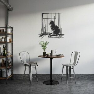 May include: A black metal cat silhouette wall art piece. The cat is sitting in front of a window. The art is mounted on a white wall above a small round table and two metal chairs. The room has a modern, minimalist design.