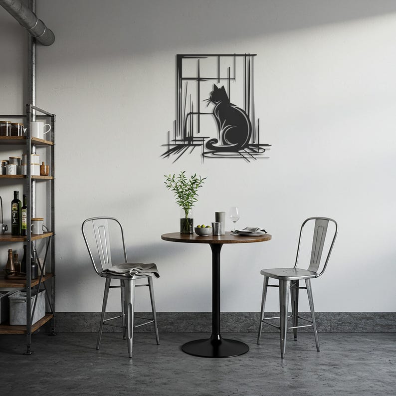 May include: A black metal cat silhouette wall art piece. The cat is sitting in front of a window. The art is mounted on a white wall above a small round table and two metal chairs. The room has a modern, minimalist design.