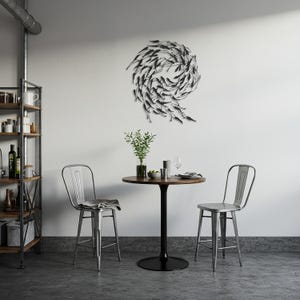 May include: A modern dining area featuring a round wooden table with a black pedestal base, two metal bar stools, and a decorative metal wall art piece depicting a school of fish. A shelf with various items is visible.