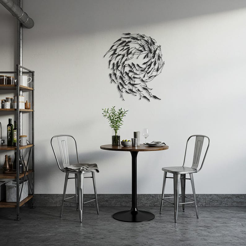 May include: A modern dining area featuring a round wooden table with a black pedestal base, two metal bar stools, and a decorative metal wall art piece depicting a school of fish. A shelf with various items is visible.