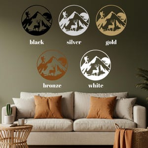 May include: Wall art featuring a mountain scene with a hiker, deer, and sun, available in black, silver, gold, bronze, and white. The circular designs are displayed above a sofa with orange throw pillows.