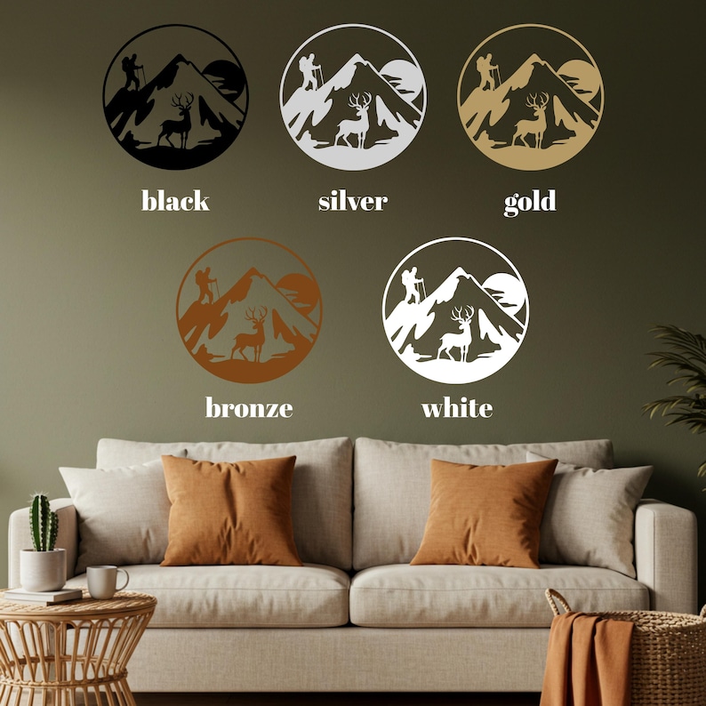 May include: Wall art featuring a mountain scene with a hiker, deer, and sun, available in black, silver, gold, bronze, and white. The circular designs are displayed above a sofa with orange throw pillows.