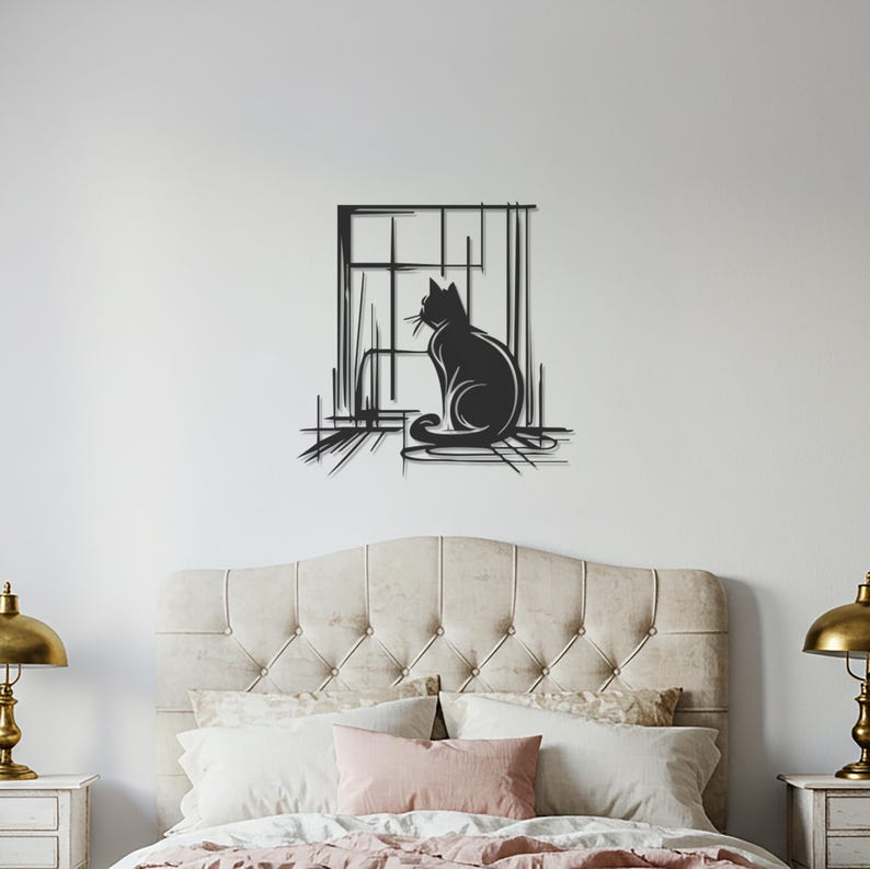 May include: A black metal wall art piece depicting a cat silhouette seated in front of a window. The cat is facing to the left, with a detailed outline. The window frame and surrounding lines add a sketched effect. The artwork is mounted on a white wall above a bed.