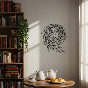 May include: A black metal wall sculpture depicting a school of fish in a swirling pattern. The artwork is mounted on a white wall. A wooden table holds white teapots, a teacup, and a plate of baked goods. A bookshelf is visible.
