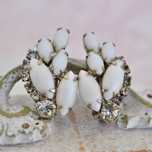 May include: A pair of white and silver clip-on earrings with a cluster of white oval-shaped stones and clear rhinestones.
