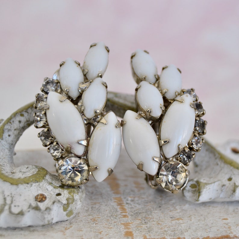 May include: A pair of white and silver clip-on earrings with a cluster of white oval-shaped stones and clear rhinestones.