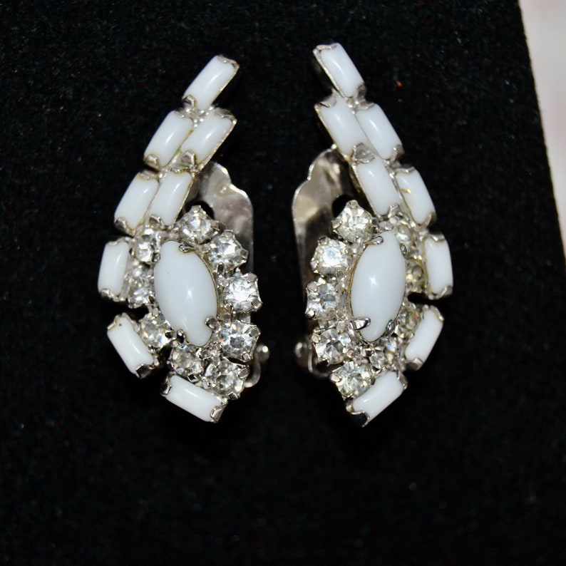 May include: A pair of white and silver clip-on earrings with a cluster of rhinestones and white oval stones.