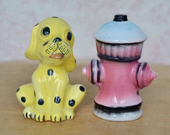 May include: A yellow ceramic dalmatian dog figurine with black spots and a pink ceramic fire hydrant figurine. Both figurines are salt and pepper shakers.
