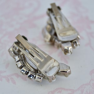 May include: A pair of silver tone clip-on earrings with a cluster of clear rhinestones in a teardrop shape.