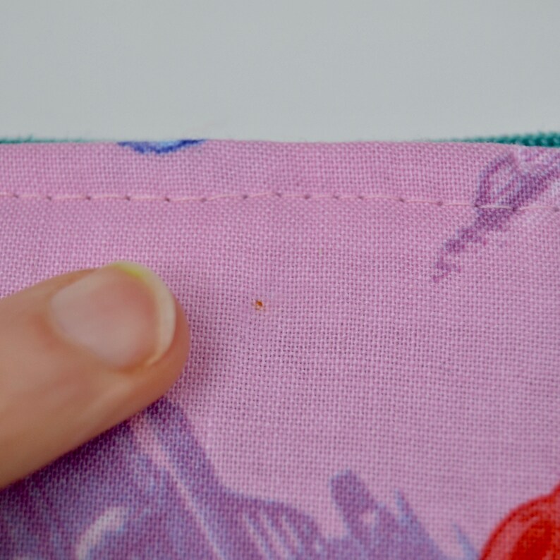 Puede incluir: Primer plano de una tela rosa con una peque&ntilde;a mancha naranja. La tela tiene un sutil patr&oacute;n de azul y morado.