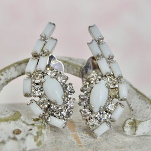 May include: A pair of white clip-on earrings with a cluster of clear rhinestones and white oval-shaped stones.