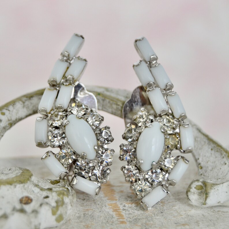 May include: A pair of white clip-on earrings with a cluster of clear rhinestones and white oval-shaped stones.