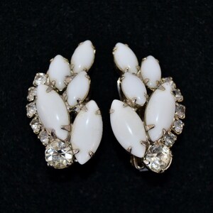 May include: A pair of white and silver clip-on earrings with a cluster of white oval-shaped stones and clear rhinestones.
