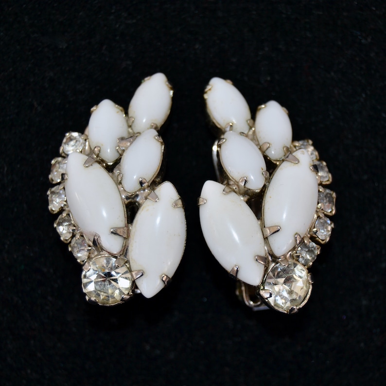 May include: A pair of white and silver clip-on earrings with a cluster of white oval-shaped stones and clear rhinestones.