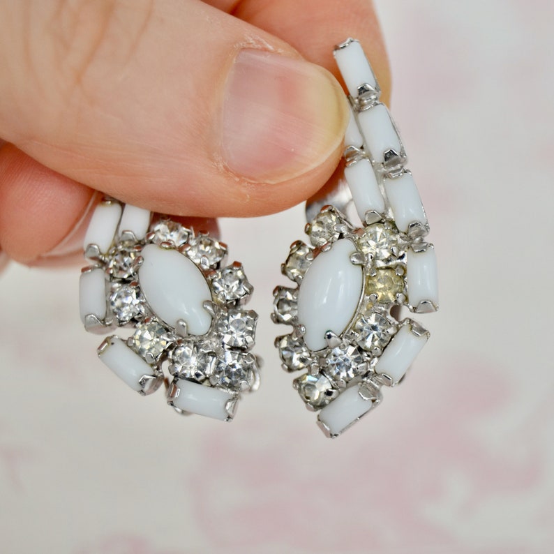 May include: A pair of white clip-on earrings with a cluster of clear rhinestones and a white oval-shaped stone in the center.