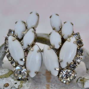 May include: A pair of white and clear crystal earrings with a cluster of oval-shaped stones. The earrings are silver-toned and have a vintage style.