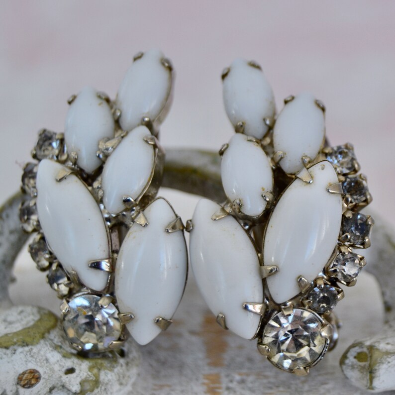 May include: A pair of white and clear crystal earrings with a cluster of oval-shaped stones. The earrings are silver-toned and have a vintage style.