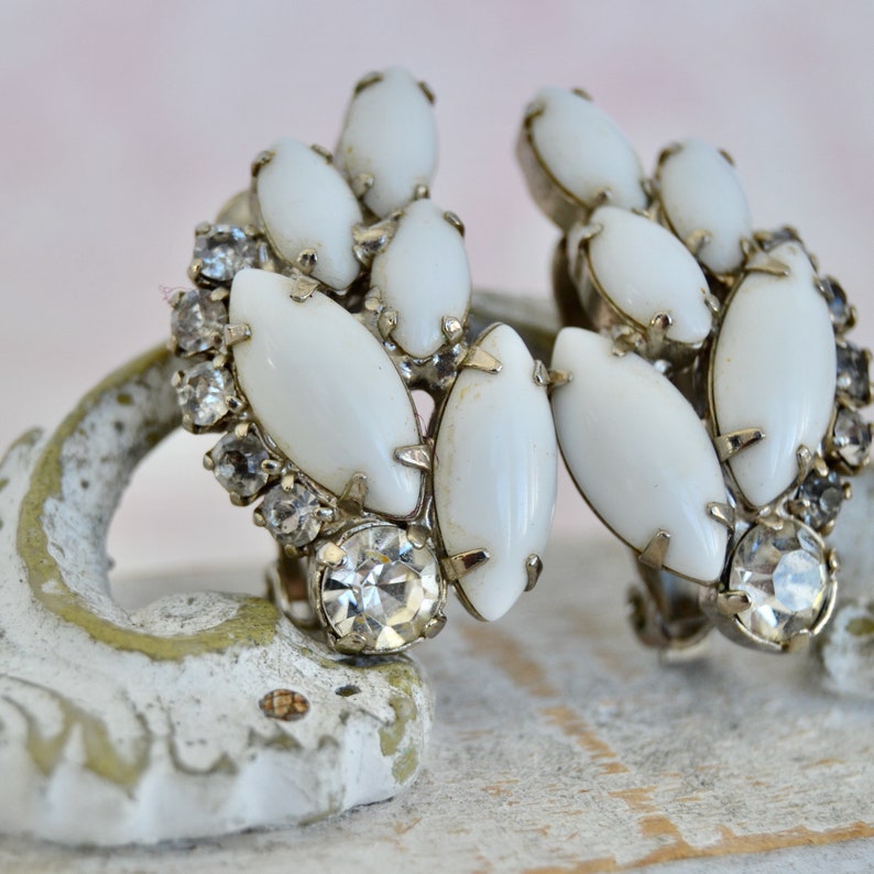 May include: A pair of white and silver clip-on earrings with a cluster of white oval-shaped stones and clear rhinestones.