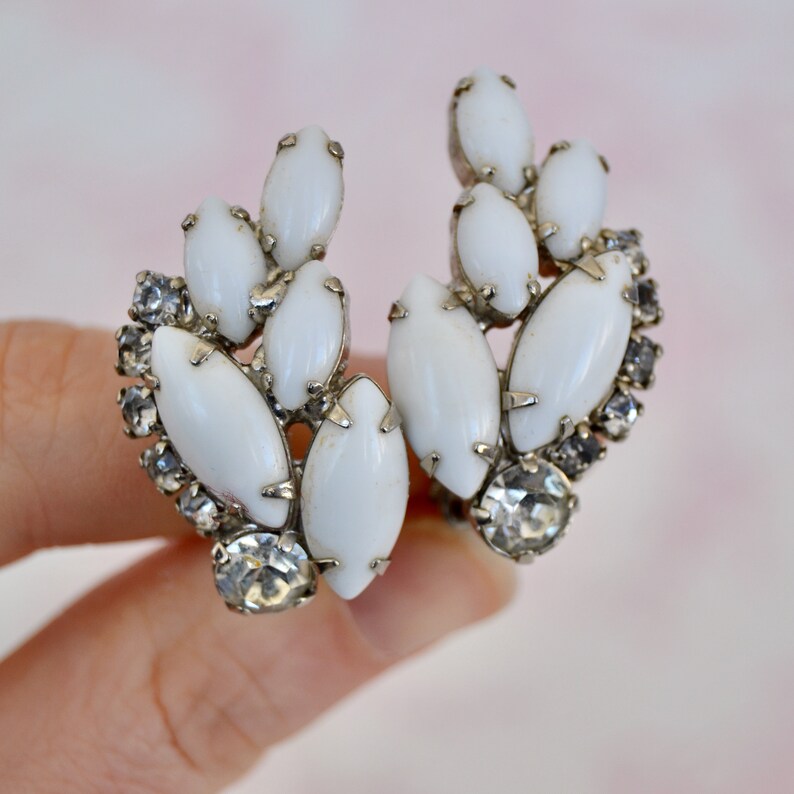 May include: A pair of white and silver clip-on earrings with a cluster of white oval-shaped stones and clear rhinestones.
