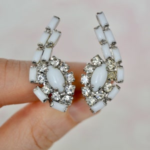 May include: A pair of white and silver clip-on earrings with a cluster of clear rhinestones and white oval stones.