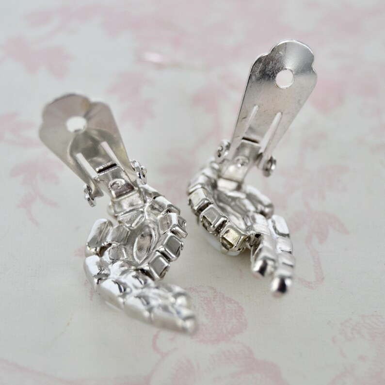 May include: A pair of silver tone clip-on earrings with clear rhinestone accents. The earrings are shaped like a wing.