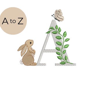 Peut inclure: Motif brodé avec la lettre "A", une vigne verte, un papillon et un lapin. Le motif comprend le texte "A to Z" dans un cercle beige. Le lapin est brun clair.